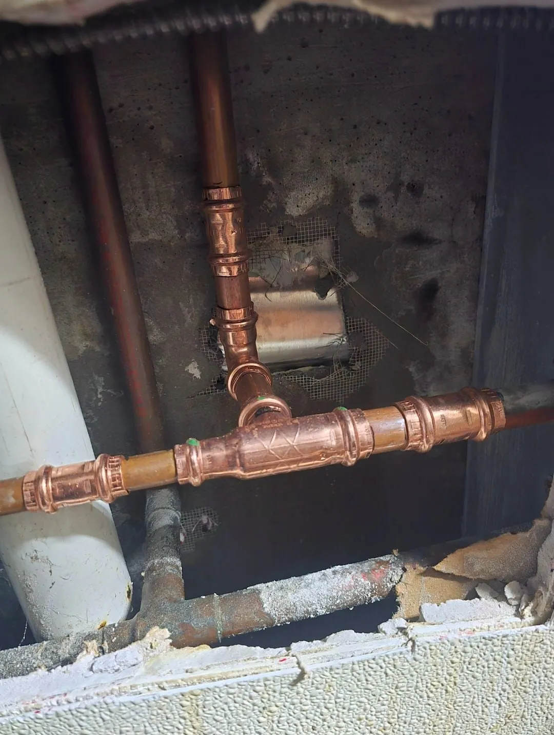 A new copper tee and press fittings joined into a water line inside an opened wall
