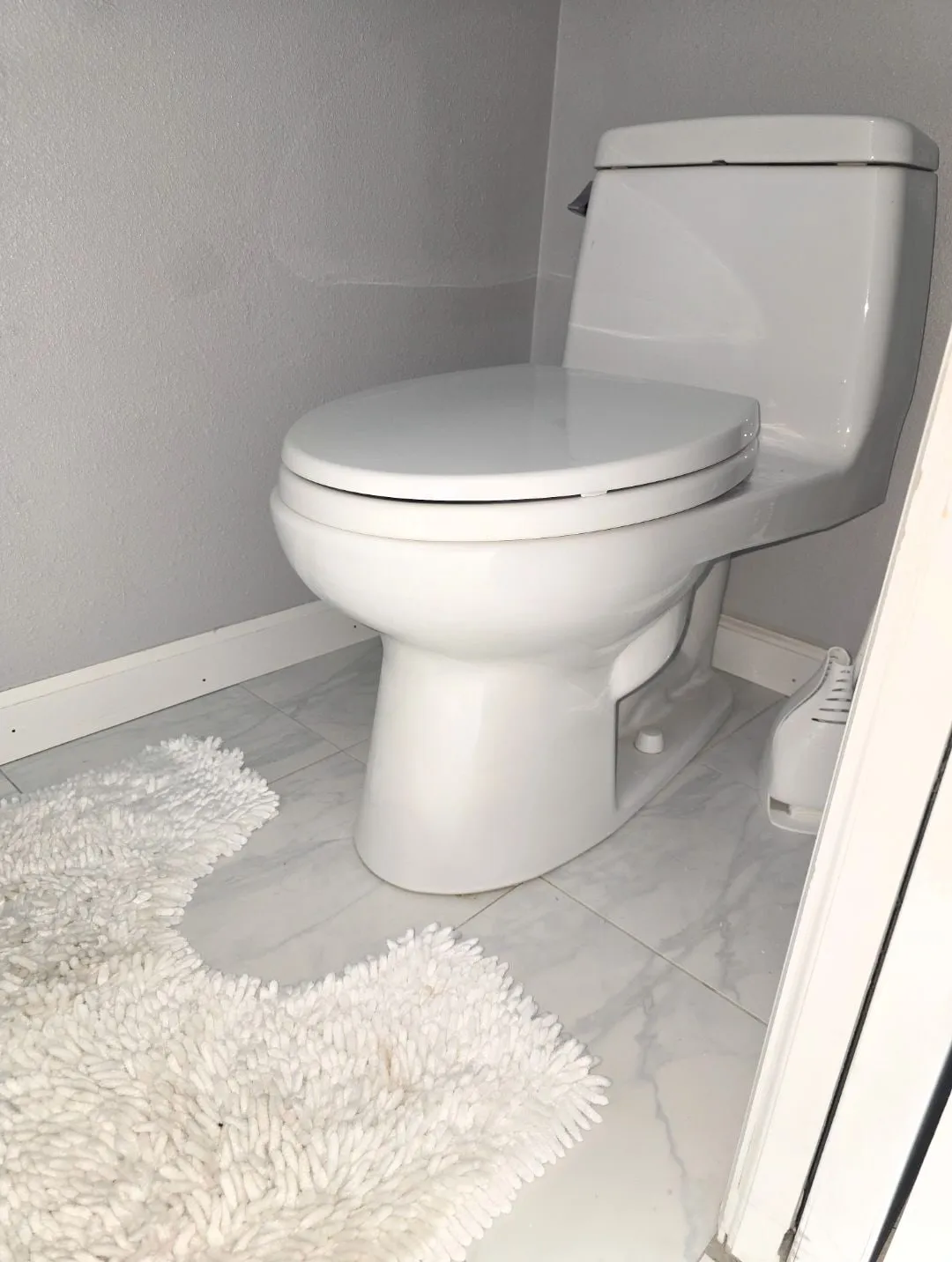 A white one-piece toilet in a gray bathroom with marble-look floor tile