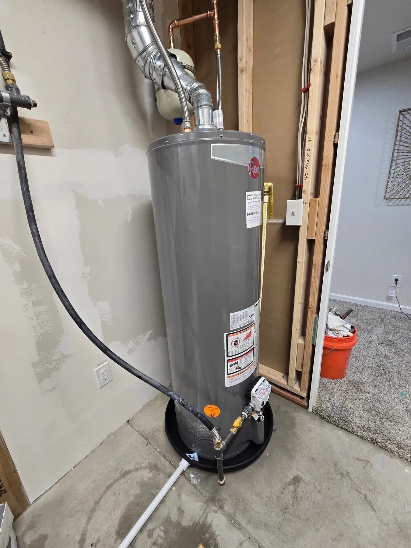 A new Rheem gas water heater sitting in a drain pan in a utility closet